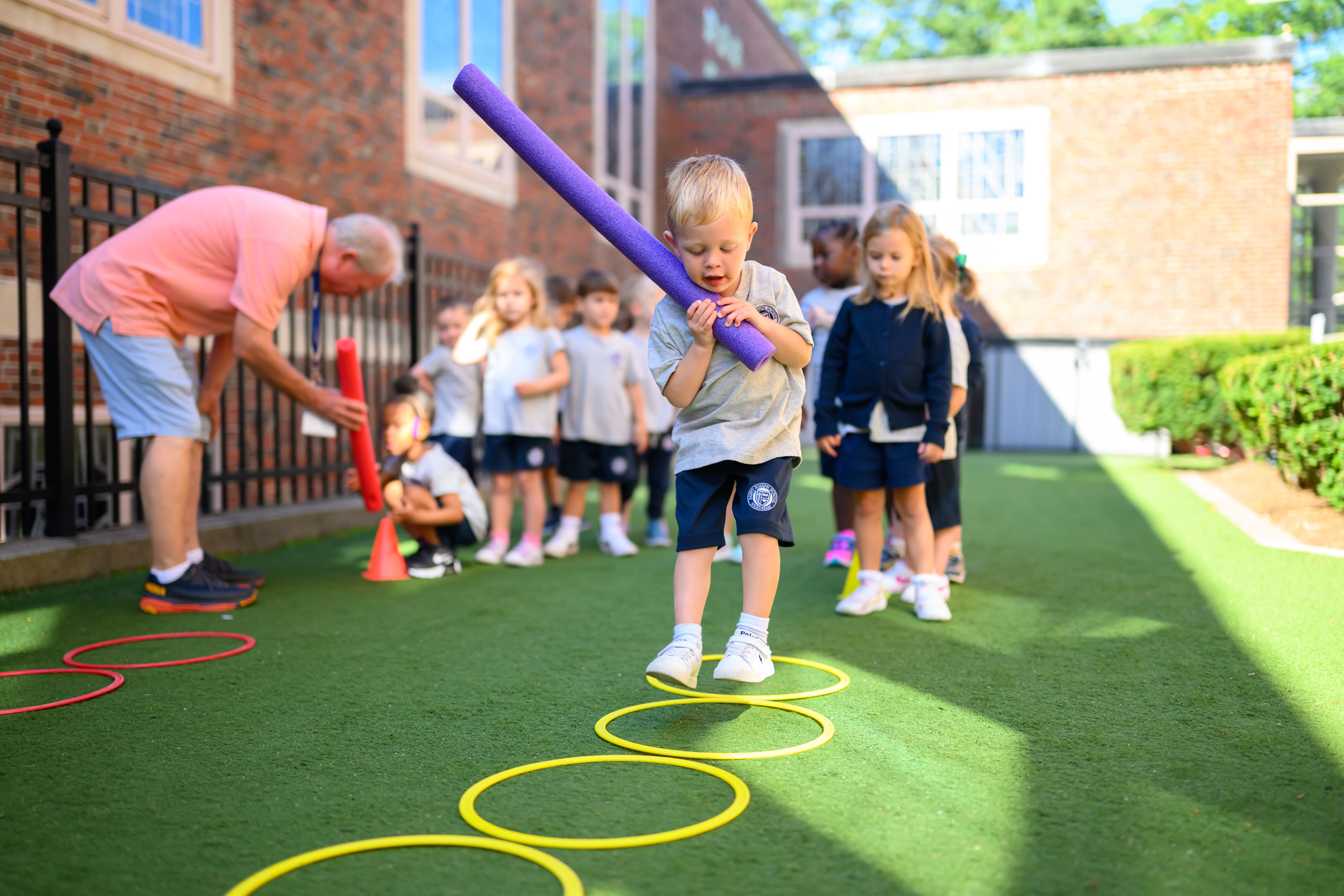 Little boy jumping into hula hoops on the ground while holding a pool noodle